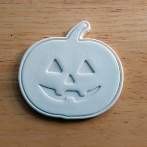 May include: White plastic pumpkin cookie cutter with a carved jack-o'-lantern face.