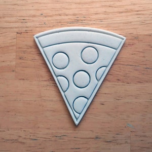 May include: White ceramic cookie cutter shaped like a slice of pizza with six pepperoni circles.