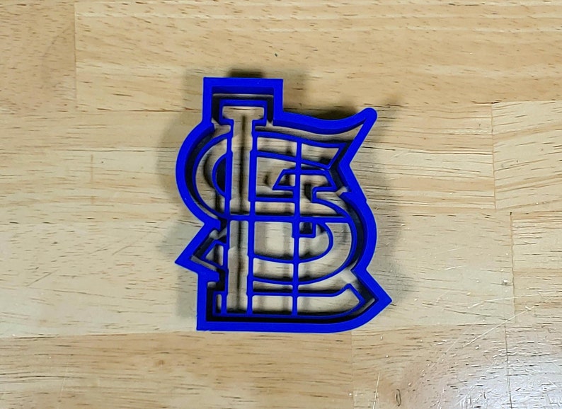 K&ouml;nnte beinhalten: Ein blauer Plastik-Ausstecher in Form des Logos der St. Louis Cardinals. Das Logo ist ein stilisiertes "STL" mit einem Baseballschl&auml;ger in der Mitte.