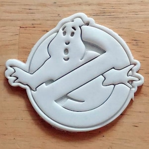 Puede incluir: Cortador de galletas de plástico blanco con forma del logotipo de Ghostbusters. El logotipo presenta un fantasma con un círculo tachado.
