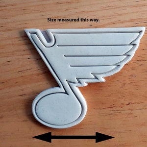 Może przedstawiać: Biała plastikowa foremka do ciasteczek w kształcie logo drużyny hokejowej St. Louis Blues. Logo to stylizowana nuta z skrzydłem na g&oacute;rze. Rozmiar mierzony w najszerszym miejscu foremki.
