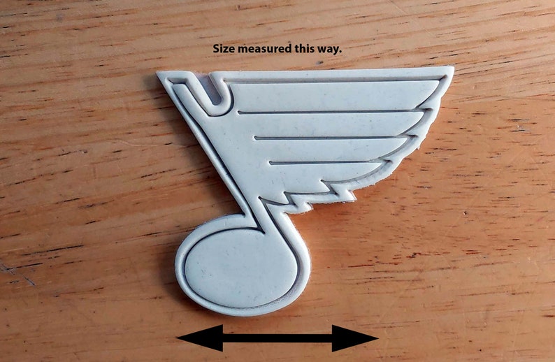Może przedstawiać: Biała plastikowa foremka do ciasteczek w kształcie logo drużyny hokejowej St. Louis Blues. Logo to stylizowana nuta z skrzydłem na g&oacute;rze. Rozmiar mierzony w najszerszym miejscu foremki.