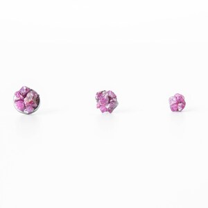 May include: Three small pink ruby gemstone earrings set in silver.