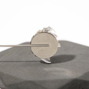May include: A silver metal disc with a clear crystal attached to the top. The disc is attached to a thin metal rod.