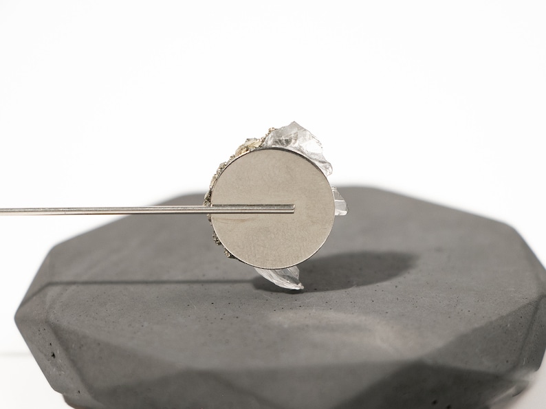 May include: A silver metal disc with a clear crystal attached to the top. The disc is attached to a thin metal rod.