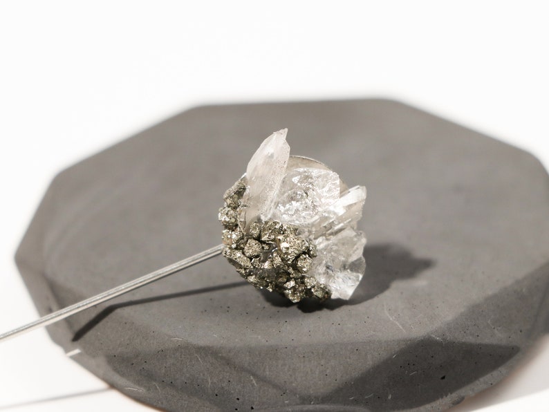 May include: A silver pin with a cluster of clear quartz crystals and a base of dark gray pyrite.