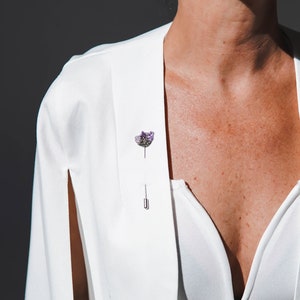 May include: A white blazer with a single amethyst crystal pin on the lapel.