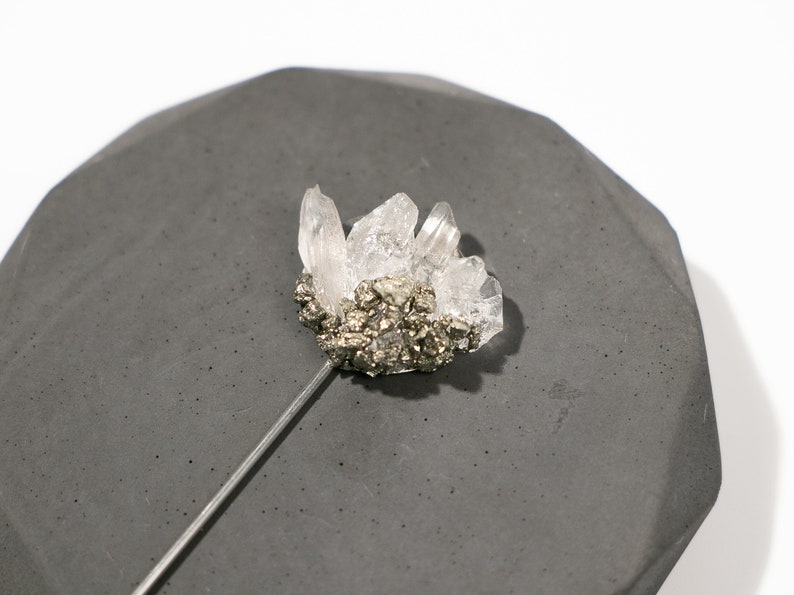 May include: A silver pin with a cluster of clear quartz crystals and a base of pyrite.