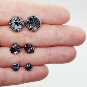 May include: Four pairs of black and silver stud earrings with different sized stones. The stones are made of a sparkly, black material.