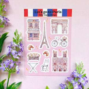 Puede incluir: Una hoja de pegatinas con monumentos y símbolos parisinos, incluyendo la Torre Eiffel, el Arco del Triunfo, la Catedral de Notre Dame, un café, una bicicleta y croissants. Las pegatinas están sobre un fondo rosa y tienen un borde blanco. El texto "Let's go to Paris" y "Only happy things" está impreso en la parte superior de la hoja.