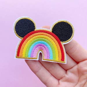 Op de afbeelding: Gestikt patch in de vorm van een regenboog met Mickey Mouse oren. De regenboog is gemaakt van rood, oranje, geel, groen, blauw, indigo en violet. De oren zijn zwart met gouden randen.
