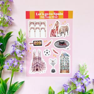 Op de afbeelding: Een vel stickers met een roze achtergrond en witte randen. De stickers bevatten illustraties van Spaanse bezienswaardigheden, eten en cultuur. De tekst "Let's go to Spain" en "Only happy things" staat in rood en geel bovenaan het vel.