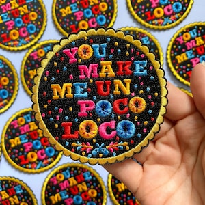 Könnte beinhalten: Ein schwarzer gestickter Aufnäher mit goldener Umrandung und einem gewellten Rand. Der Aufnäher zeigt den Text "You make me un poco loco" in bunten Buchstaben auf einem Konfetti-ähnlichen Hintergrund.