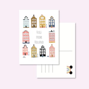 Peut inclure: Une carte postale avec des illustrations de maisons hollandaises colorées. Le texte "Hugs From Holland" est au centre. Le verso de la carte postale est vierge avec des lignes pour écrire et un petit motif arc-en-ciel.