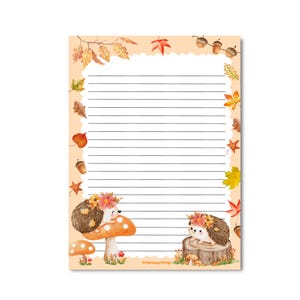 Op de afbeelding: Een rechthoekig vel briefpapier met horizontale zwarte lijnen en een geschulpte witte rand. De achtergrond bevat aquarel herfstbladeren, eikels, twee egels met bloemenkransen, paddenstoelen en een boomstronk. De tekst luidt Onlyhappythings.