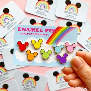 Op de afbeelding: Set van zes emaillepins met een cartoon muizenkop silhouet in verschillende kleuren: rood, geel, oranje, groen, blauw en paars. De pins worden getoond op een kaart met een regenboog en de tekst "ENAMEL PIN @ONLYHAPPYTHINGS."