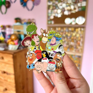 May include: A gold-colored enamel pin featuring a group of characters from the Toy Story franchise. The characters include Woody, Buzz Lightyear, Jessie, Rex, Mr. and Mrs. Potato Head, Hamm, Slinky Dog, and others. The pin is a fun and collectible item for fans of the Toy Story movies.