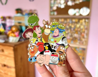 Puede incluir: Un pin de esmalte dorado con un grupo de personajes de la franquicia Toy Story. Los personajes incluyen a Woody, Buzz Lightyear, Jessie, Rex, el Sr. y la Sra. Potato Head, Hamm, Slinky Dog y otros. El pin es un artículo divertido y coleccionable para los fanáticos de las películas de Toy Story.