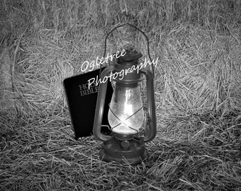 A Bible  Beside  a Coal Oil Lamp Sitting on a Bale of Hay