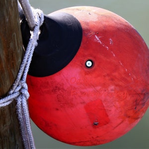Könnte beinhalten: Eine rote und schwarze Boje mit einem Seil darum gebunden. Die Boje ist an einem Holzpfosten befestigt.