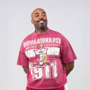 以下が含まれることがあります： 「KAPPA ALPHA PSI UNIVERSITY INDIANA 1911」の白文字が入った、マルーン色の半袖シャツ。卒業キャップをかぶった人物が描かれた紋章の、使い古されたグラフィックが特徴です。ヴィンテージスタイルです。