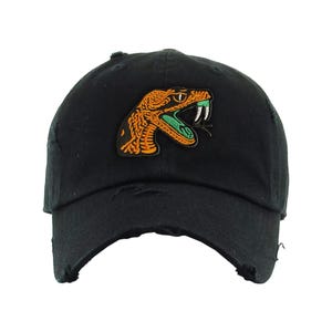 May include: Black baseball cap with a distressed brim, featuring an embroidered patch of an orange and green snake with white fangs. The snake is in a striking, open-mouthed pose.