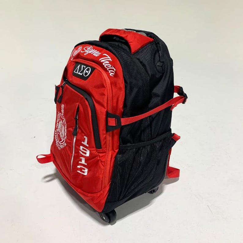 May include: A red and black rolling backpack featuring the text Delta Sigma Theta, the Greek letters &Delta;&Sigma;&Theta;, and the number 1913 in white embroidery. The bag includes a top handle, side compression straps, black mesh side pockets, and wheels at the base.