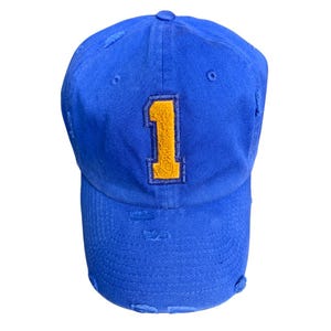 May include: A blue distressed baseball cap with a yellow number one embroidered on the front.