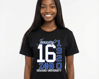 May include: Black t-shirt with the text "January 16 1920" in white and blue, along with "ZΦB O" and "HOWARD UNIVERSITY". The shirt is worn by a person with long black hair.