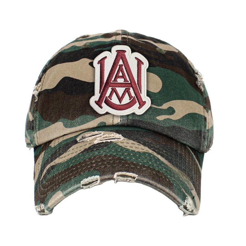 May include: Camouflage baseball cap with a distressed brim. The cap features a patch with the letters "A" and "M" in maroon, outlined in white. The hat is in shades of green, brown, and tan.