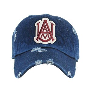 May include: A distressed denim baseball cap with a white patch featuring the letters "A" and "M" in a burgundy outline. The cap has a pre-worn look with frayed edges and a curved brim.
