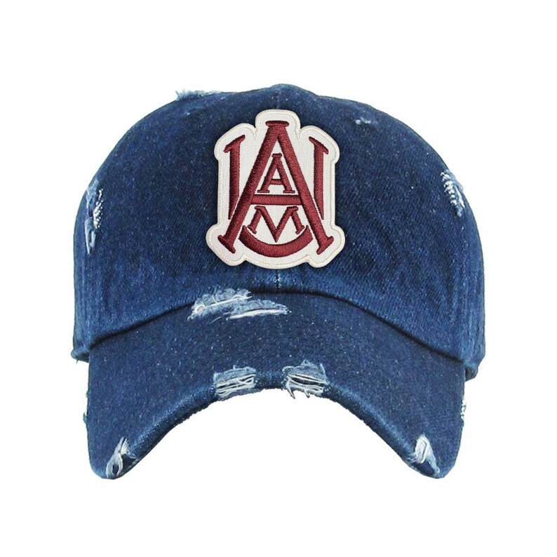May include: A distressed denim baseball cap with a white patch featuring the letters "A" and "M" in a burgundy outline. The cap has a pre-worn look with frayed edges and a curved brim.