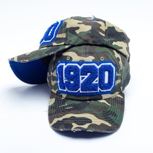 May include: A camouflage baseball cap with a blue and white "1920" patch on the front.