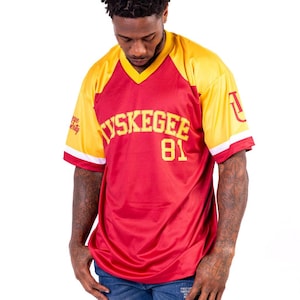May include: A red and yellow jersey with the text "TUSKEGEE 81" on the front. The jersey has a white trim around the sleeves and collar.
