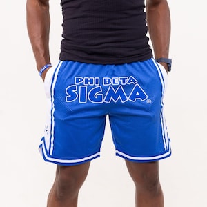May include: Blue mesh shorts with white accents and the text "PHI BETA SIGMA" in white. The shorts have a drawstring waist and are knee-length. The shorts are made of a breathable material.