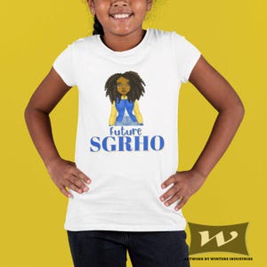 May include: White t-shirt with a graphic of a girl with curly hair and a blue top. The text "Future SGRHO" is printed in blue below the graphic. The shirt is worn by a person with dark hair and skin.