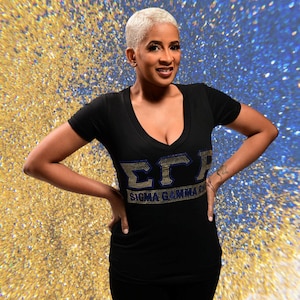 May include: A black v-neck t-shirt with a gold and blue rhinestone design that reads "ΣΓΡ Sigma Gamma Rho".