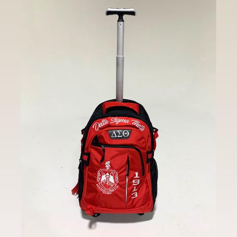 May include: A red and black rolling backpack with an extended silver telescopic handle. The bag features the white embroidered text Delta Sigma Theta, the Greek letters &Delta;&Sigma;&Theta;, the number 1913, and a white crest logo on the front red panel.