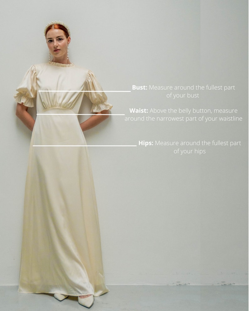May include: A woman wearing a white satin dress with a ruffled neckline and sleeves. The dress has a fitted bodice and a flowing skirt. The woman is standing in front of a white wall with text describing how to measure bust, waist, and hips.