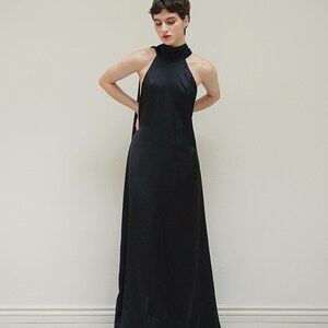 May include: A woman wearing a black halter-neck maxi dress with a high neckline.