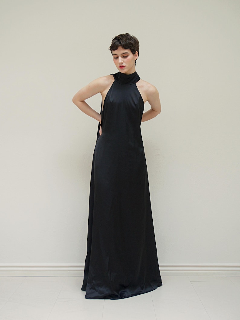 May include: A woman wearing a black halter-neck maxi dress with a high neckline.
