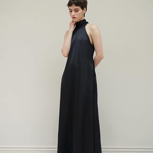 May include: A black halter-neck maxi dress with a high neckline. The dress is made of a smooth, silky fabric and has a flowing silhouette.