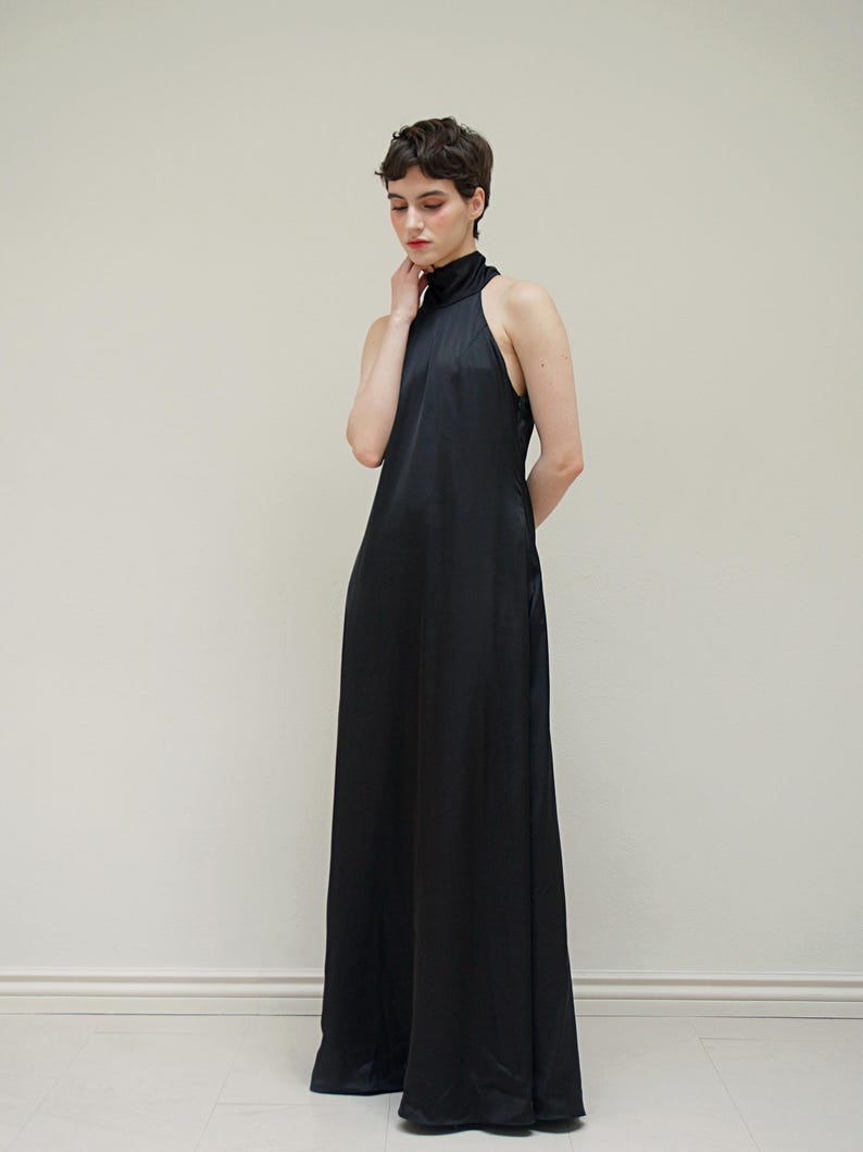 May include: A black halter-neck maxi dress with a high neckline. The dress is made of a smooth, silky fabric and has a flowing silhouette.