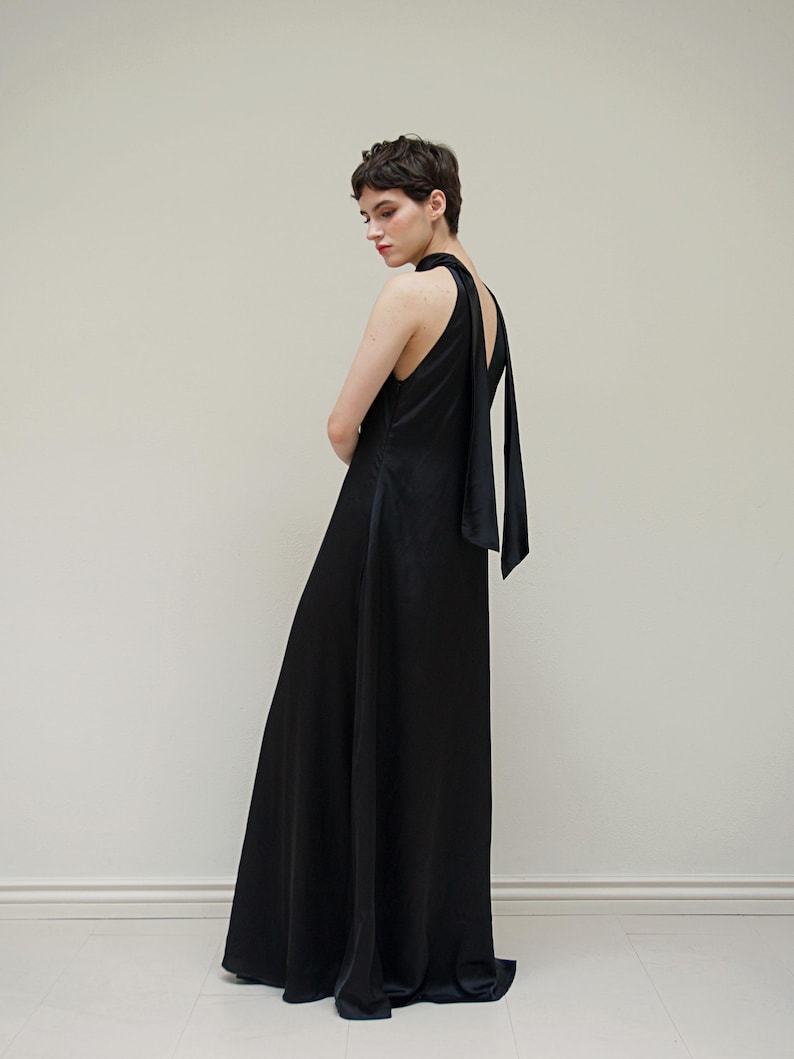 May include: A black maxi dress with a halter neckline and a long, flowing skirt. The dress has a tie at the back of the neck.