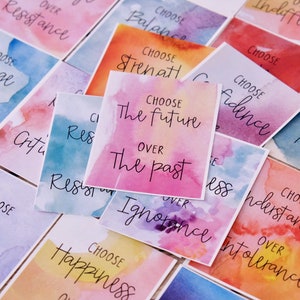 May include: A set of colourful watercolour cards with inspirational messages. Each card features a different colour scheme and a handwritten message encouraging the viewer to choose one thing over another. For example, one card says "Choose the future over the past".
