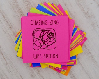 May include: A stack of colorful sticky notes with a pink note on top that says "Chasing Zing Life Edition" with a black doodle of a tangled line.