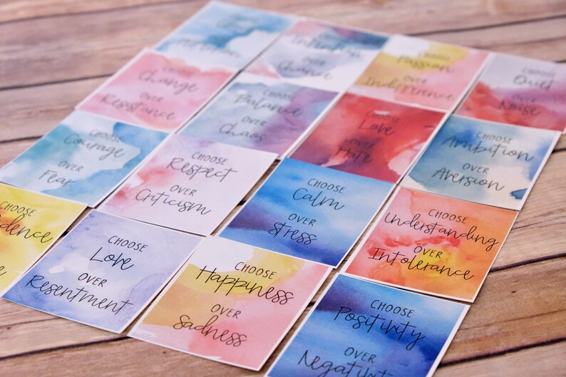 May include: A set of colourful affirmation cards with watercolour backgrounds. Each card features a positive message, such as "Choose Love over Resentment" and "Choose Happiness over Sadness".