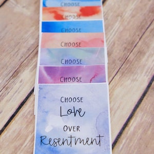 May include: A stack of colourful cards with the words "Choose Love Over Resentment" on the bottom card. The cards have a watercolour background.
