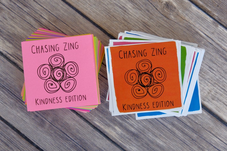K&ouml;nnte beinhalten: Zwei Stapel bunter Karten mit dem Text "Chasing Zing Kindness Edition" und einem schwarzen und wei&szlig;en Wirbeldesign.