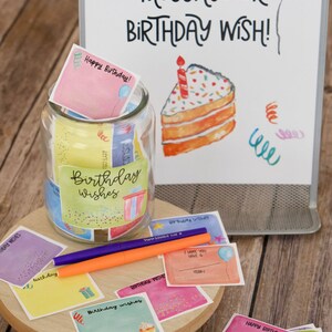 May include: A glass jar filled with colorful cards that say "Birthday Wishes" on them. The jar is surrounded by more cards with birthday wishes and a sign that says "Share a message or birthday wish!"